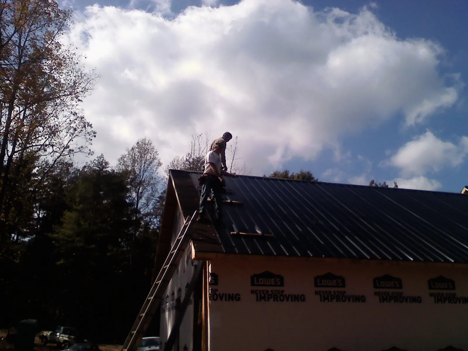 Roofer fastening dark metal panels high against a cloudy sky, from a Roof Inspection job in Mount Tremper