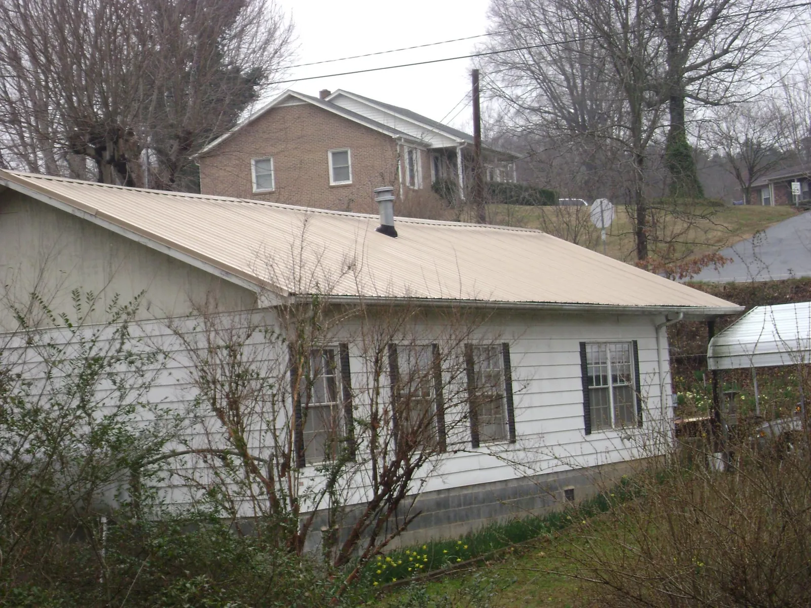 Tan metal roof on a white sided house set into a hillside — Commercial Roofing by Roofing Brothers in Mount Tremper